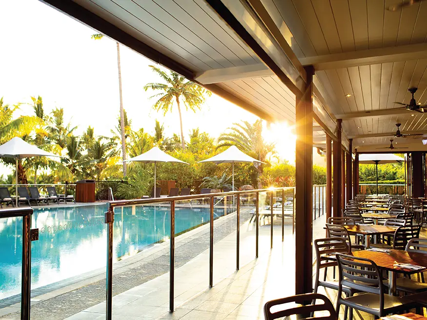 Outdoor dining by a pool with loungers at sunset.