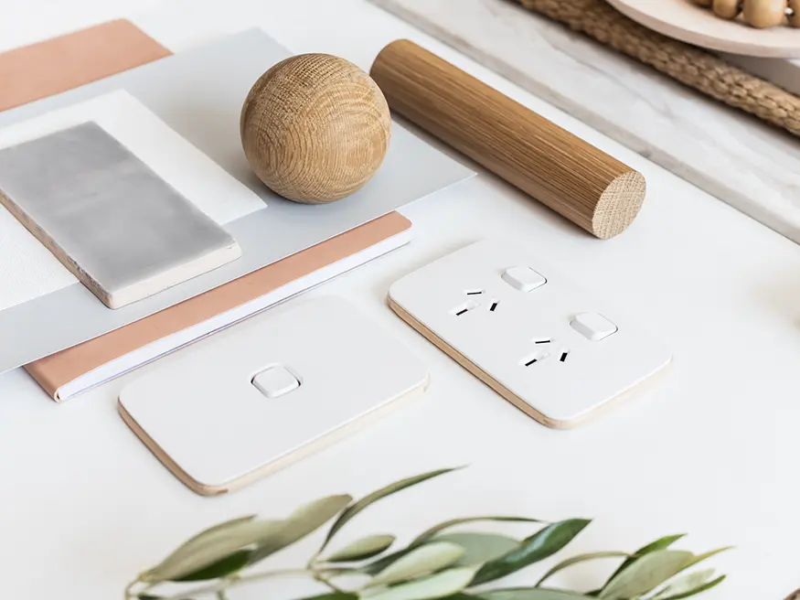 Close-up of two Vivid white Iconic switches and power points placed on a table beside wooden items and scattered papers.