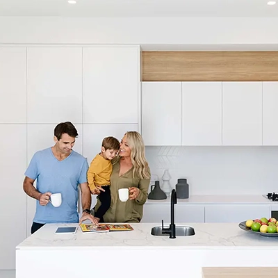 Two adults standing in a modern white kitchen with a child, holding mugs at the island bench.