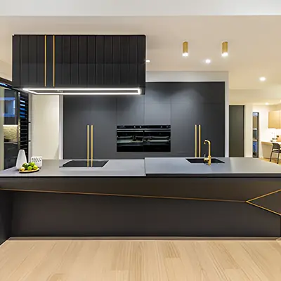 Modern kitchen with black cabinets, gold accents, island sink, two stovetops, and built-in ovens.
